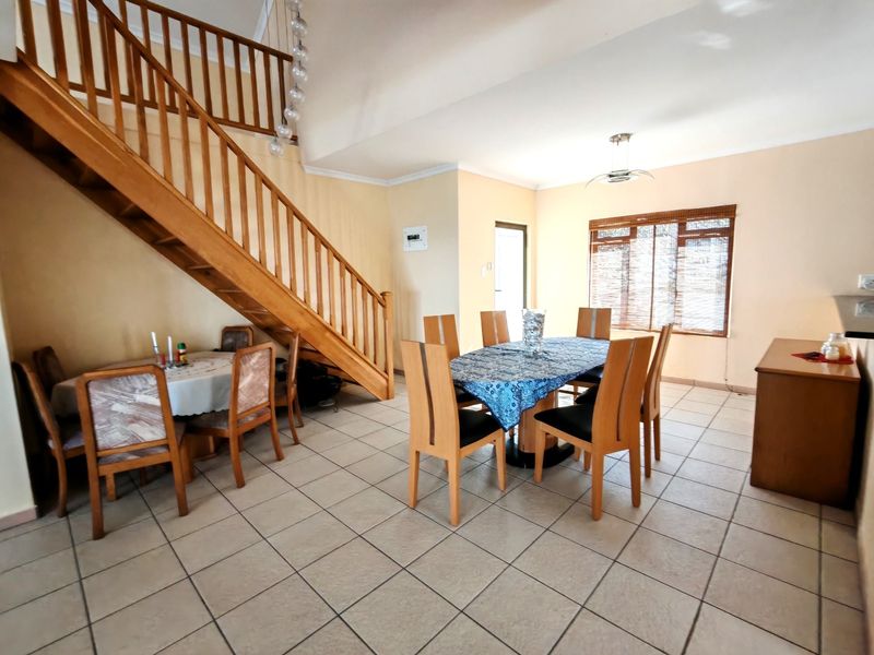 Open-plan dining area featuring tiled flooring and a prominent wooden staircase with a matching balustrade.