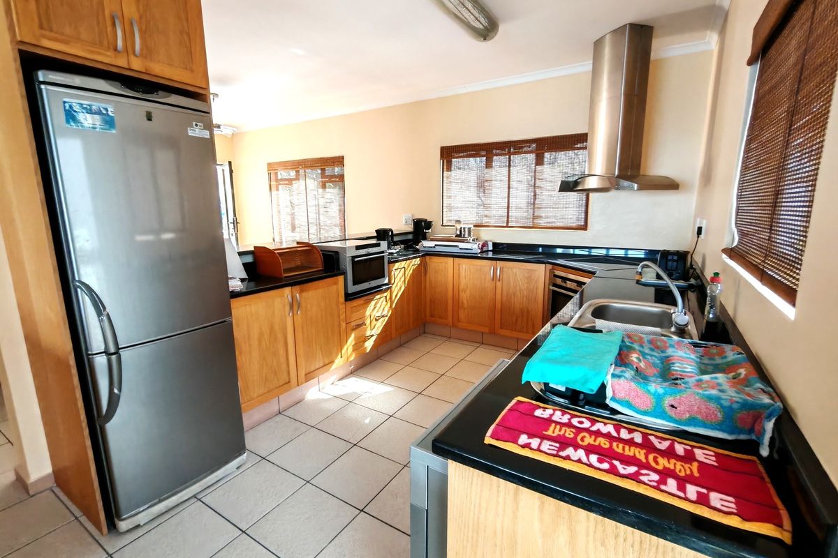 A functional kitchen featuring wooden cabinetry, granite countertops, a stainless steel extractor fan, and tiled flooring.