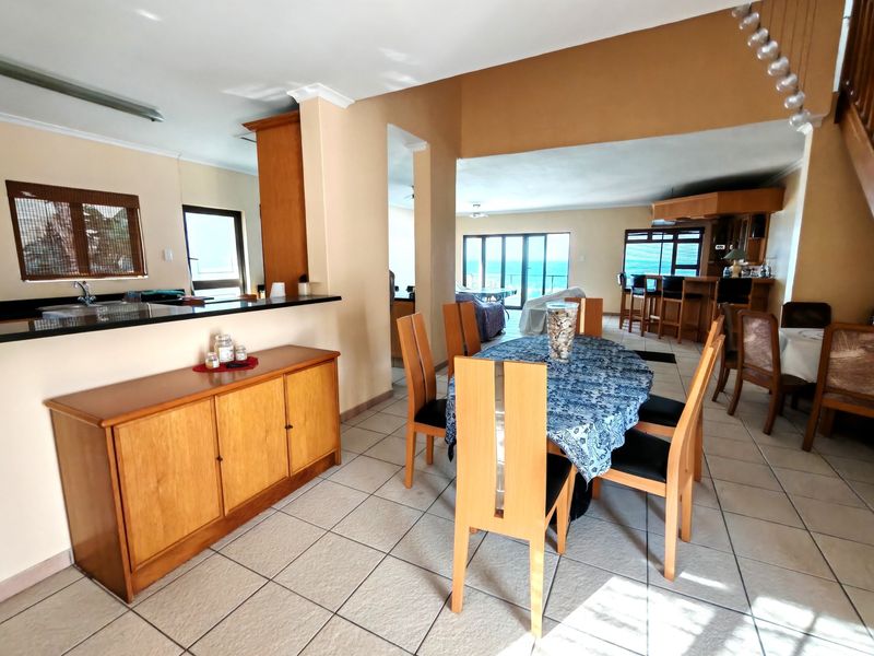 Spacious open-plan living and dining area featuring tiled floors, a kitchen breakfast bar, and a built-in bar, with direct access to a scenic balcony.