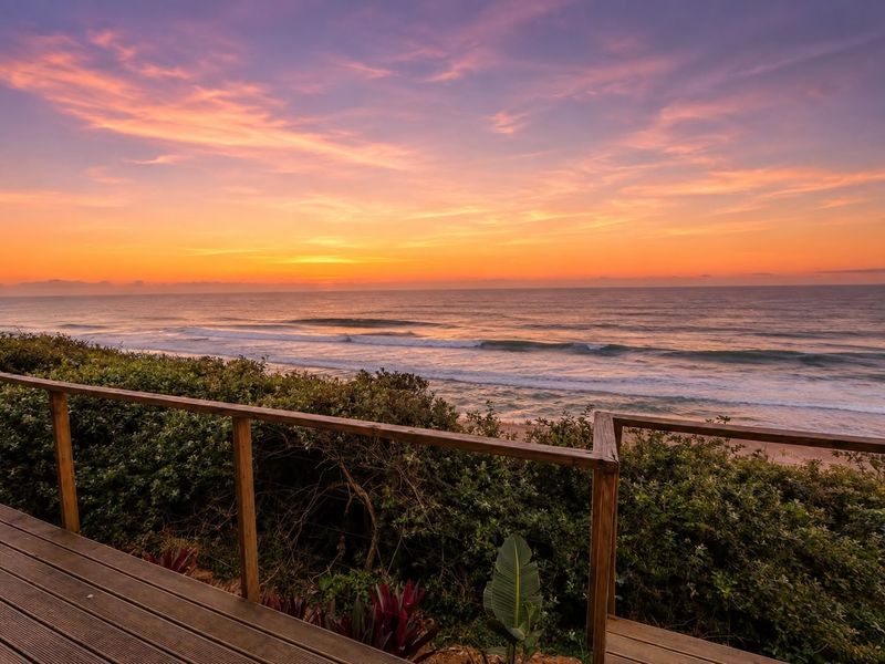 Stunning elevated ocean view from a timber deck, capturing a vibrant sunset over the coastline.