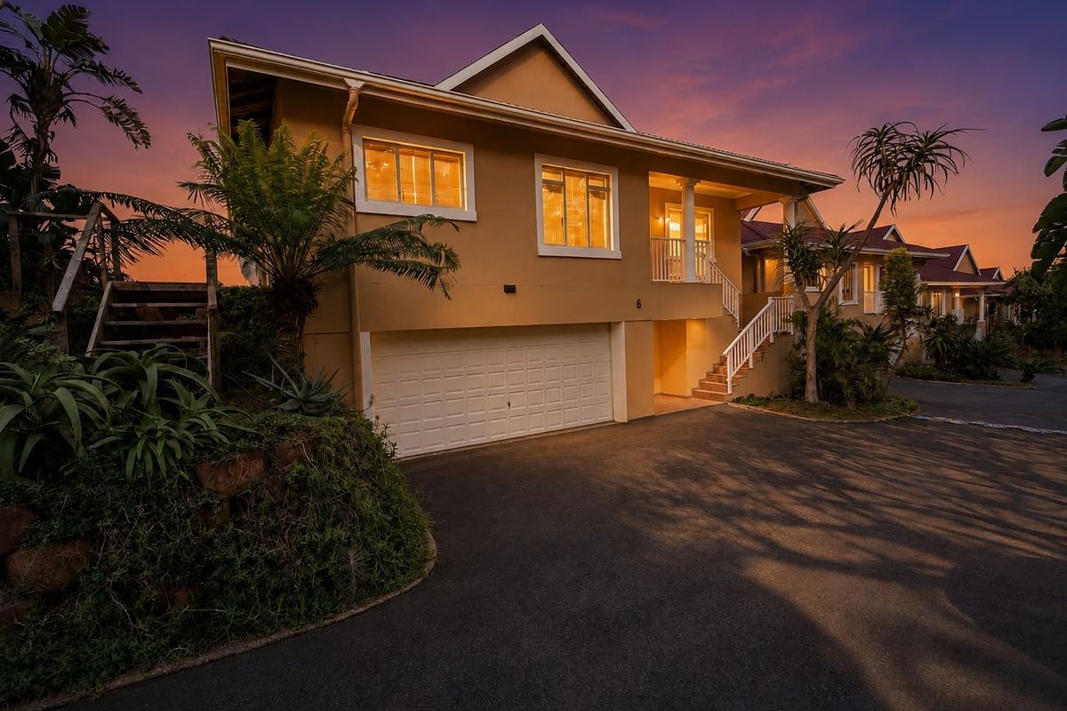 Front elevation of a multi-level residential property featuring a double garage, external staircase leading to a balcony, and a paved driveway at dusk.
