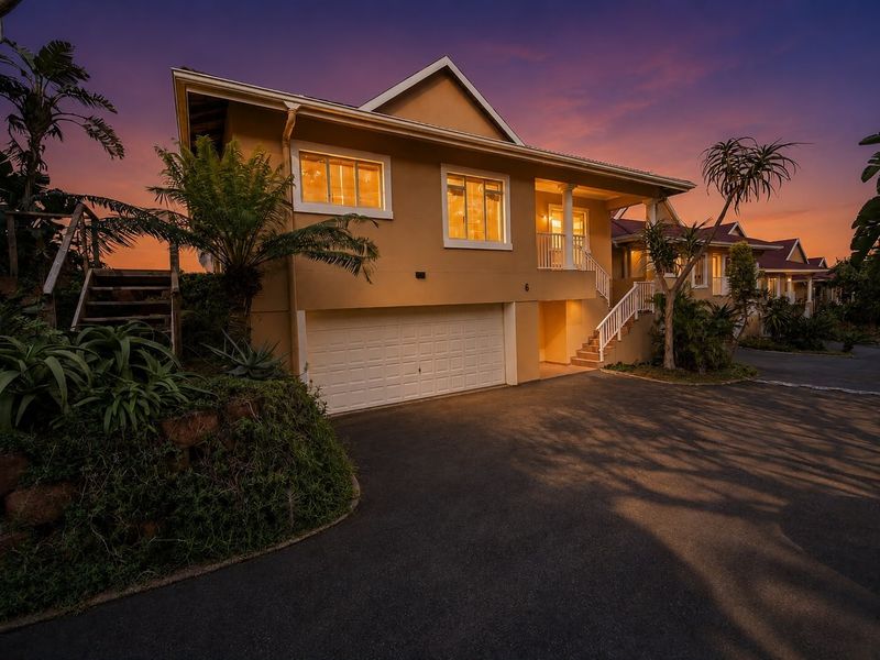 Front elevation of a multi-level residential property featuring a double garage, external staircase leading to a balcony, and a paved driveway at dusk.