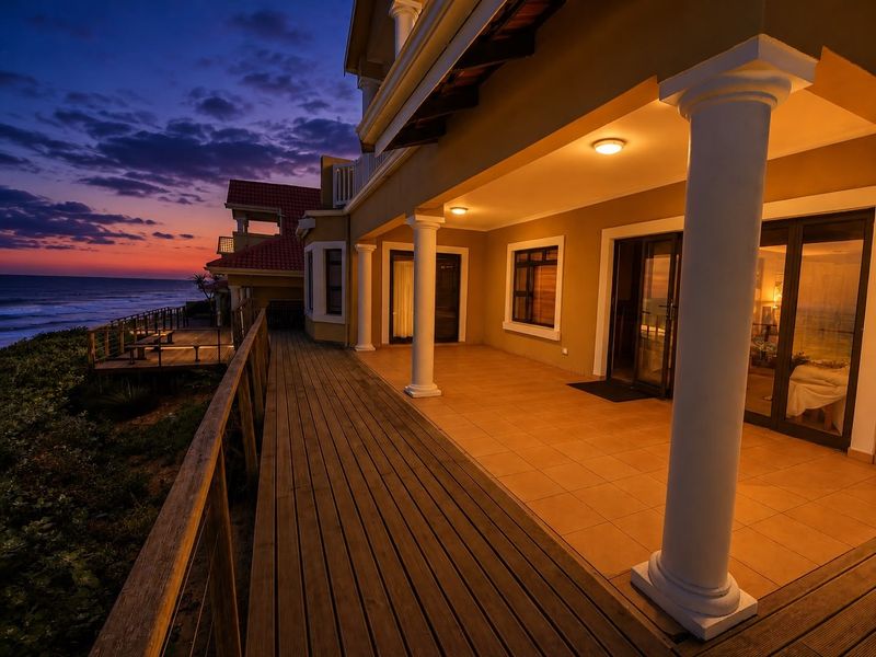 Spacious covered patio featuring tiled flooring, classical columns, and wooden decking, offering direct access to the home and scenic ocean views at sunset.