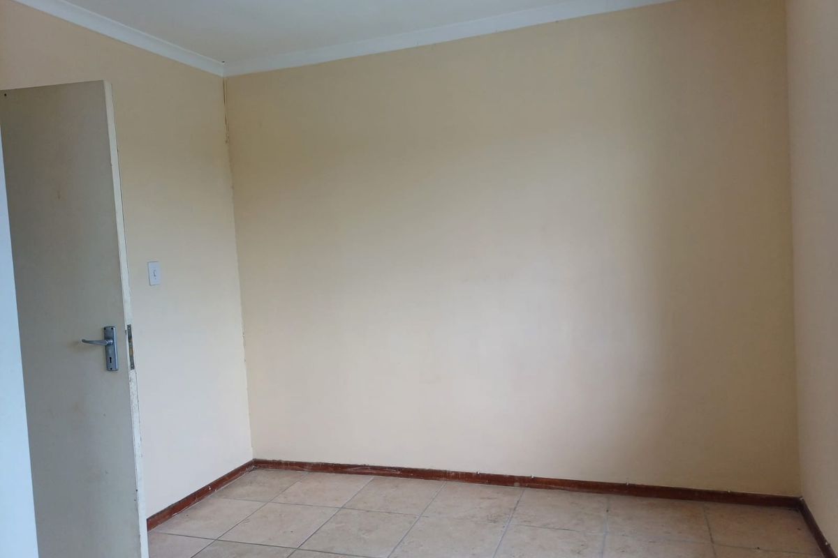 An empty bedroom featuring tiled flooring, coving, and a standard internal door, presenting a blank canvas for potential renovation or interior design updates.