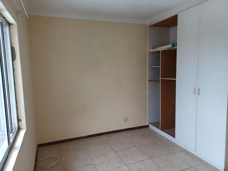 An empty bedroom featuring tiled flooring, a built-in wardrobe with one missing door, and an aluminium window frame.