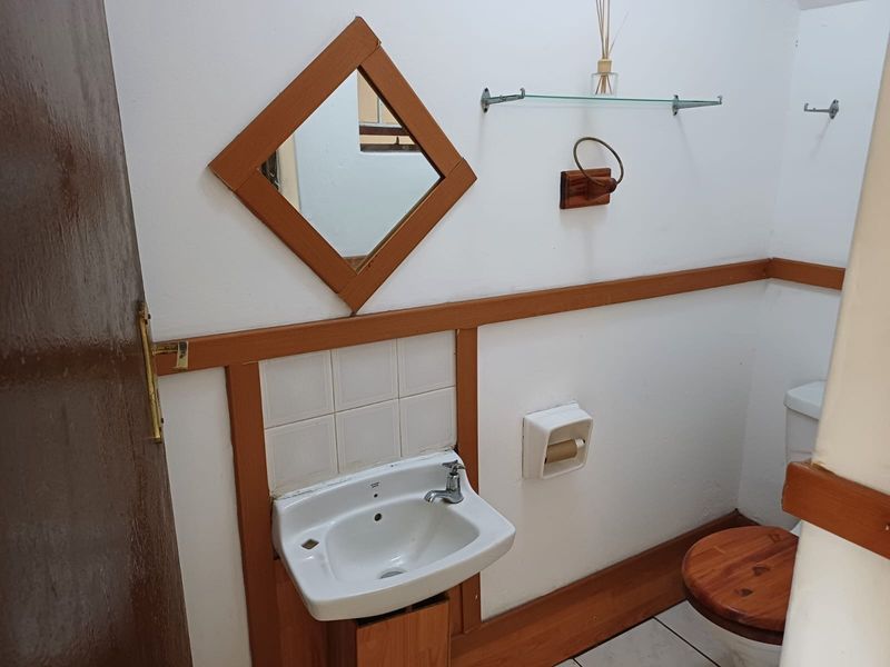A compact bathroom featuring a wall-mounted basin, tiled splashback, and wooden trim accents, providing a functional space with dated finishes.
