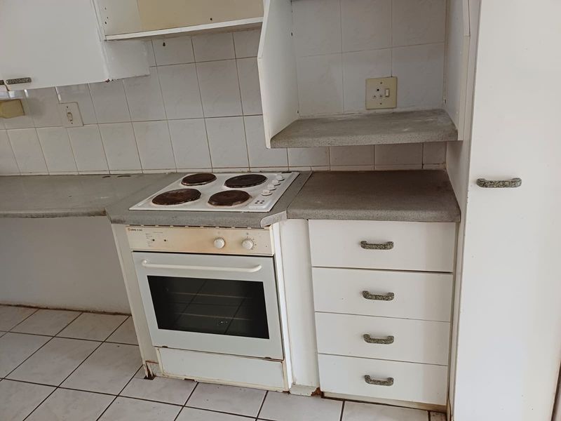 A dated kitchen area featuring a built-in oven, electric hob, tiled backsplash, and white cabinetry, requiring cosmetic updates to modernize the space.