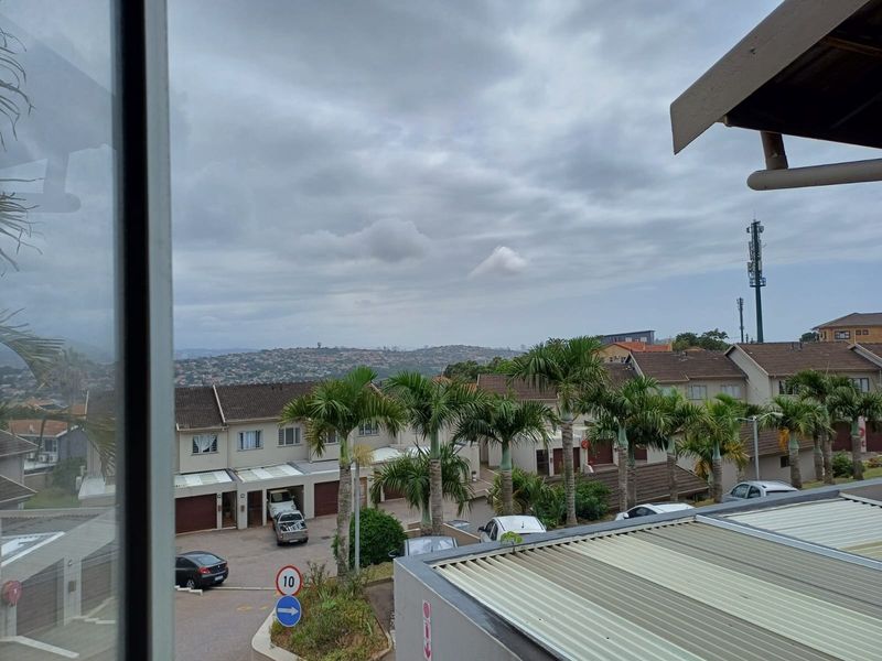 Elevated view overlooking a residential townhouse complex with paved driveways, garage access, and established palm trees under a cloudy sky.