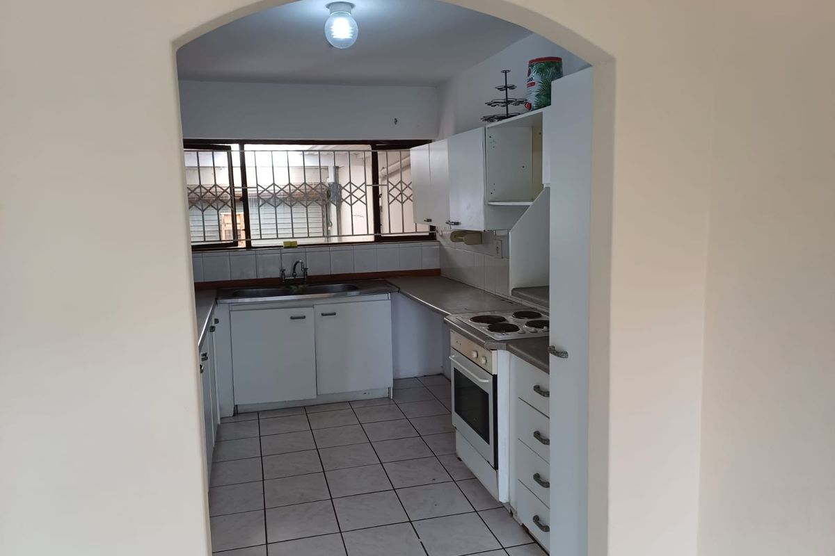 A functional kitchen featuring built-in cabinetry, a stainless steel sink, and an integrated electric stove and oven, with tiled flooring throughout.