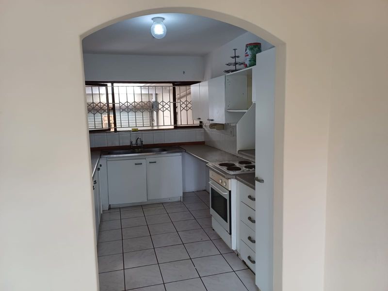A functional kitchen featuring built-in cabinetry, a stainless steel sink, and an integrated electric stove and oven, with tiled flooring throughout.