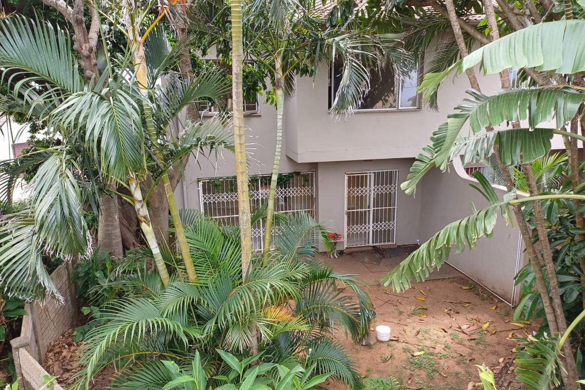 Rear view of the townhouse featuring a private garden area, security gates, and established trees providing shade and privacy.