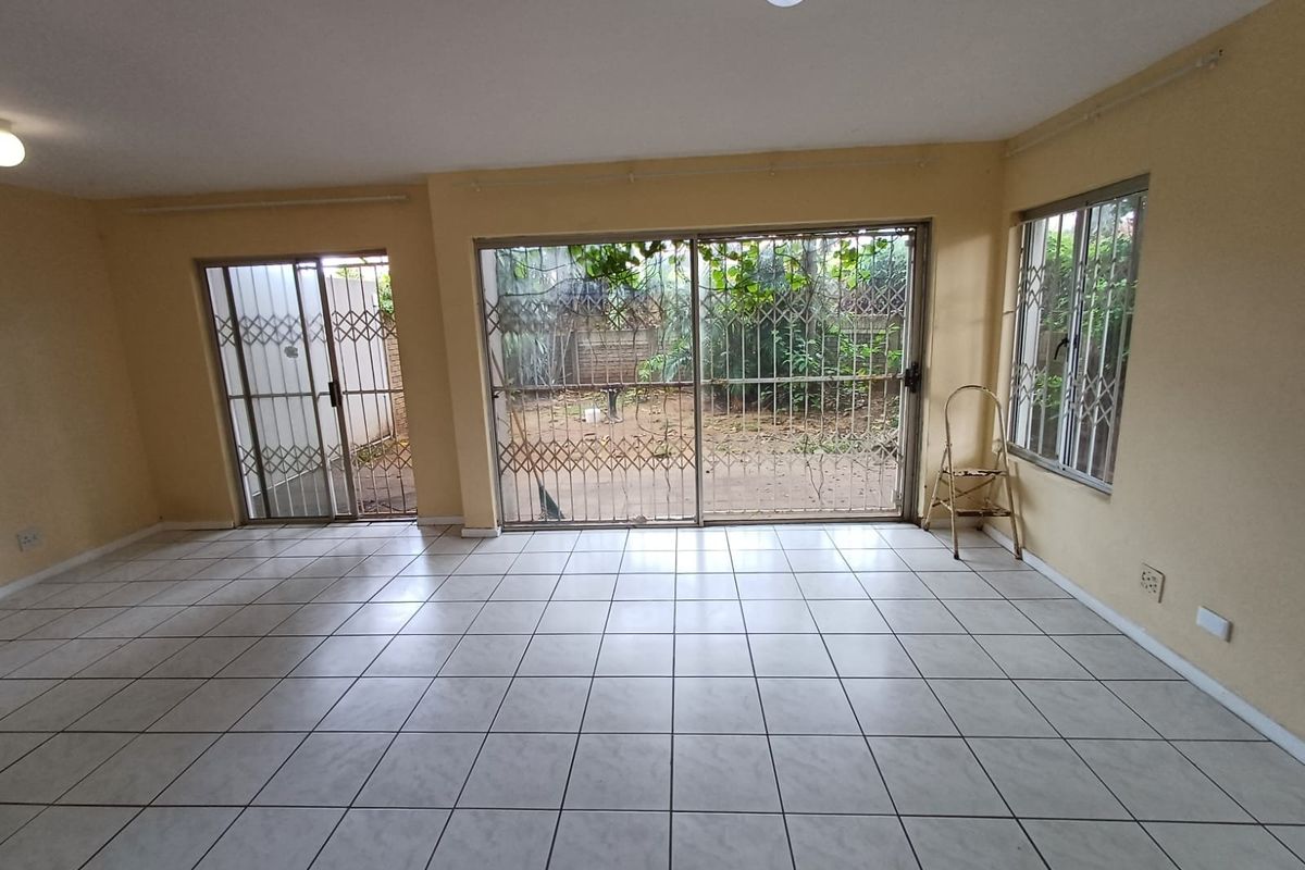 An empty living room featuring ceramic floor tiles, sliding glass doors with security gates, and direct access to the rear garden area.