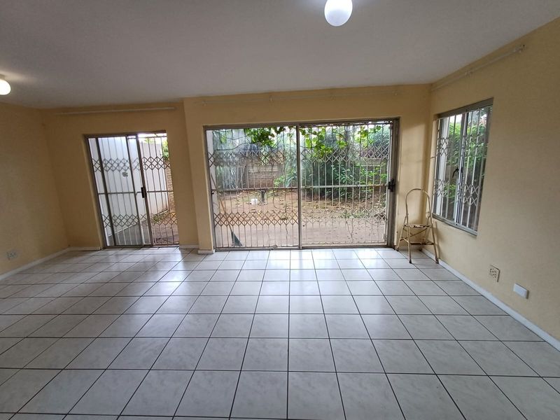 An empty living room featuring ceramic floor tiles, sliding glass doors with security gates, and direct access to the rear garden area.