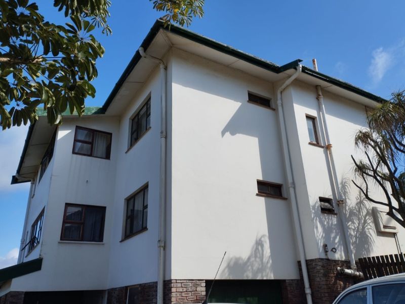 Rear elevation of a multi-story residential building featuring plastered walls, brick base detailing, and aluminium window frames under a pitched roof.