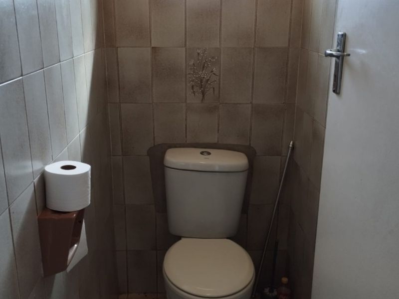 A compact, dated bathroom featuring a standard toilet, tiled walls, and tiled flooring, requiring cosmetic updates to improve its overall condition.