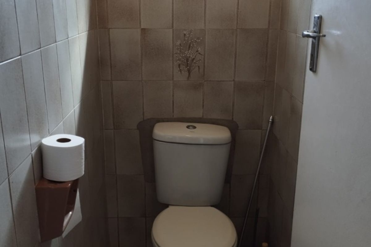 A compact, dated bathroom featuring a standard toilet, tiled walls, and tiled flooring, requiring cosmetic updates to improve its overall condition.