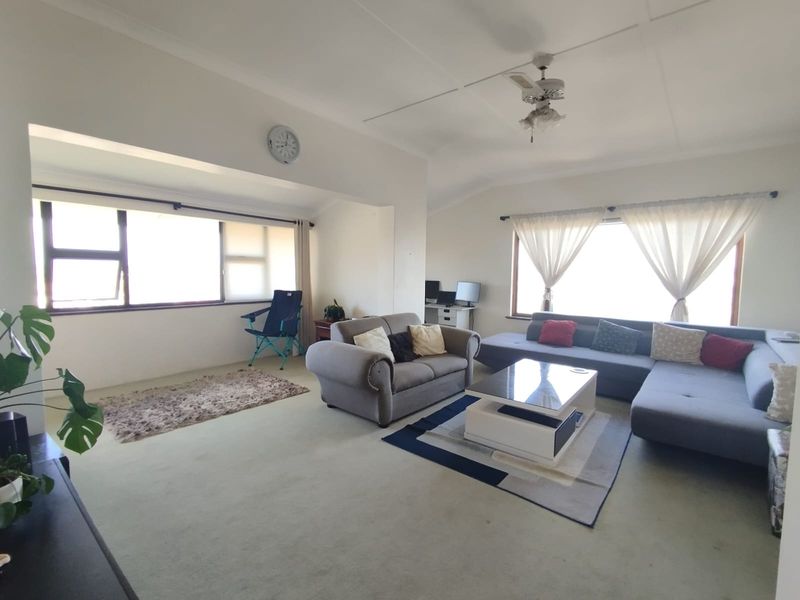Spacious living room featuring large windows, neutral wall finishes, and a ceiling fan, offering a bright and versatile layout for comfortable family living.