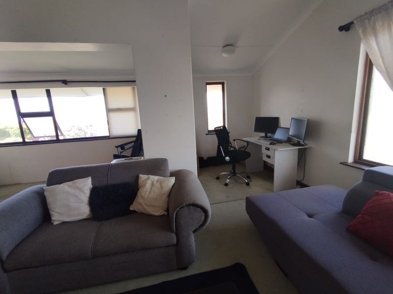 Open plan living area featuring carpeted flooring, aluminium window frames, and a dedicated workspace nook, offering a versatile layout for living and home office use.