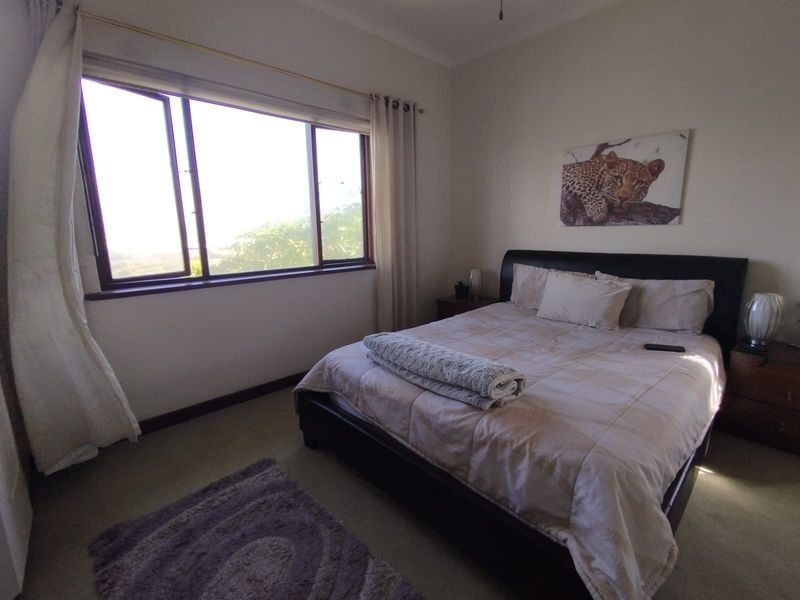 A comfortable bedroom featuring carpeted flooring, a ceiling fan, and a large casement window providing natural light and exterior views.
