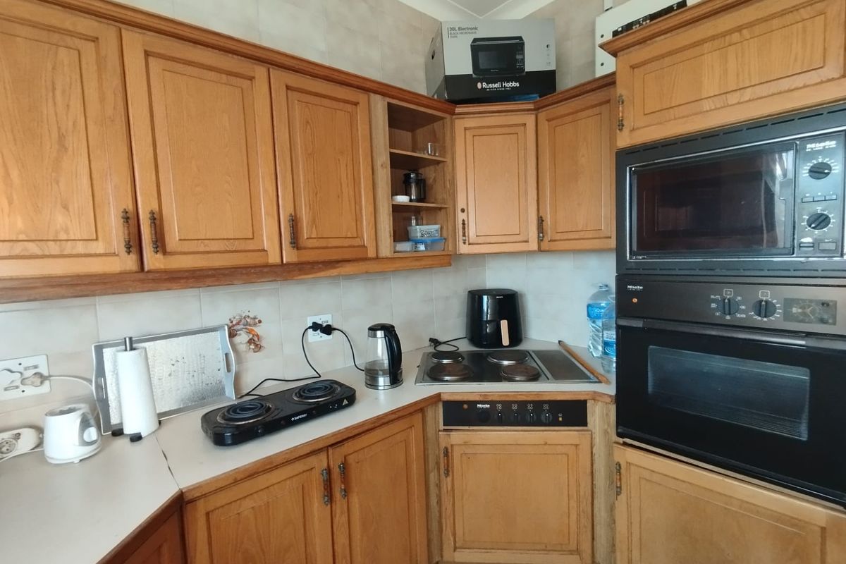 A functional kitchen featuring traditional wooden cabinetry, a built-in Miele oven and microwave, and a corner ceramic hob with tiled backsplash.