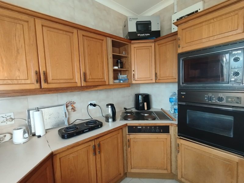A functional kitchen featuring traditional wooden cabinetry, a built-in Miele oven and microwave, and a corner ceramic hob with tiled backsplash.