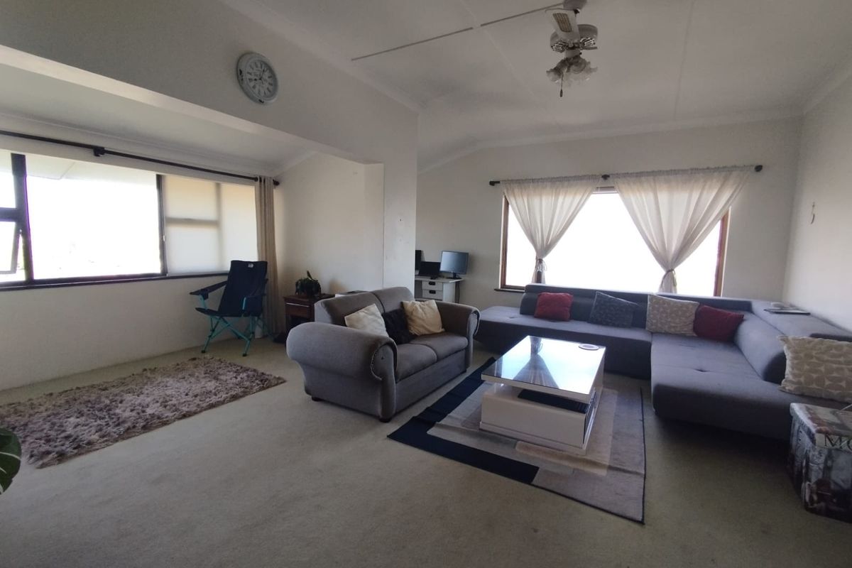 Spacious living room featuring large windows that provide ample natural light, carpeted flooring, and a ceiling fan.