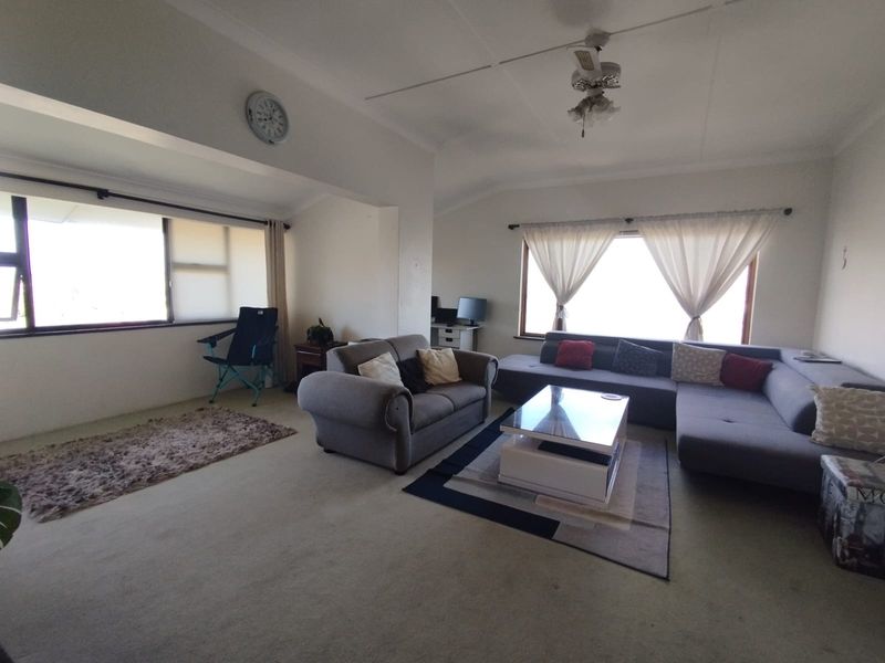 Spacious living room featuring large windows that provide ample natural light, carpeted flooring, and a ceiling fan.