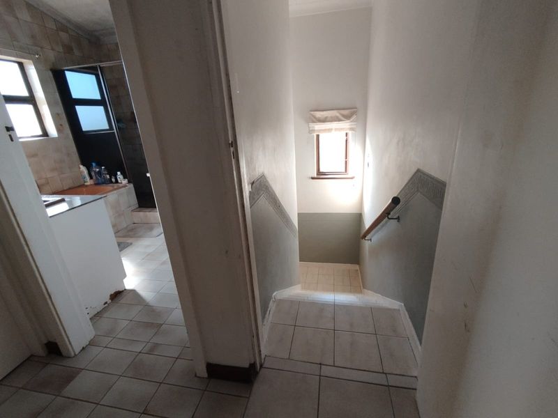 A functional hallway area featuring tiled flooring and a staircase with a handrail, leading towards a bathroom space.