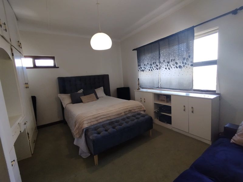 A bedroom featuring built-in storage cupboards, a pendant light fixture, and carpeted flooring, offering a functional space with potential for cosmetic updates.