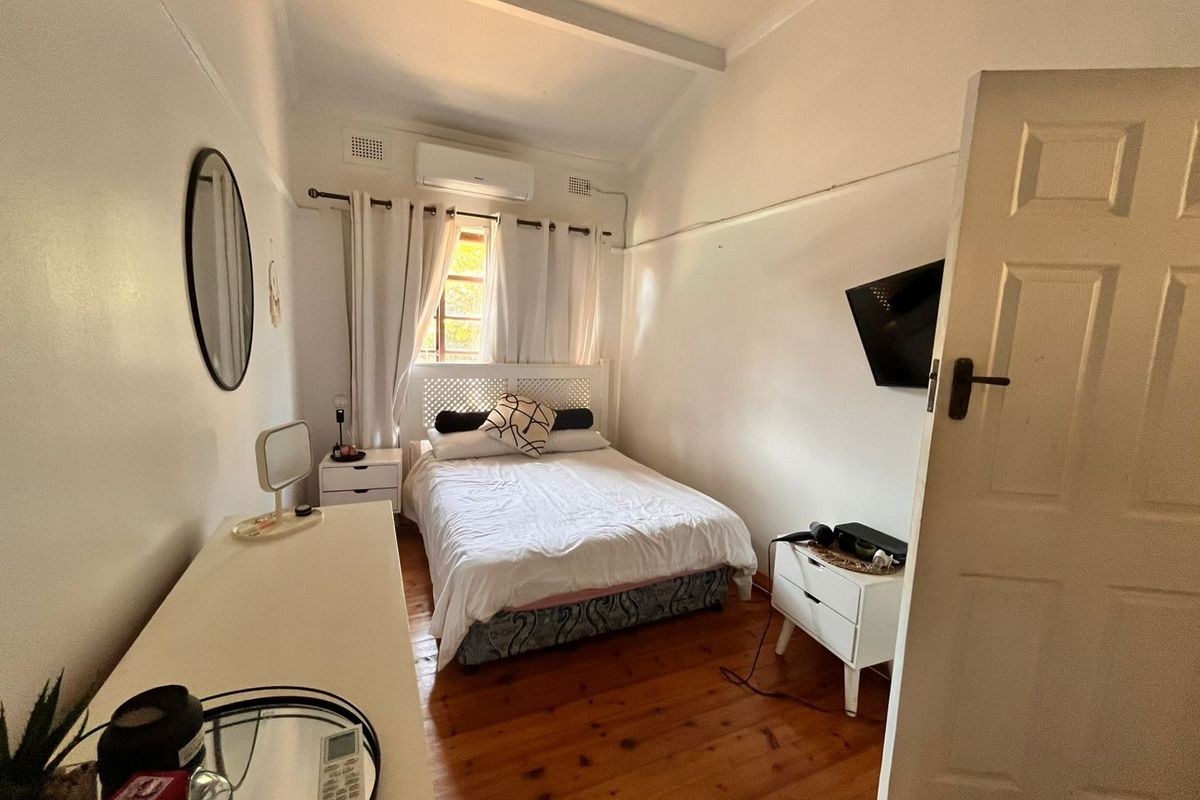 A cozy bedroom featuring polished timber flooring, a wall-mounted air conditioning unit, and classic panel door access.