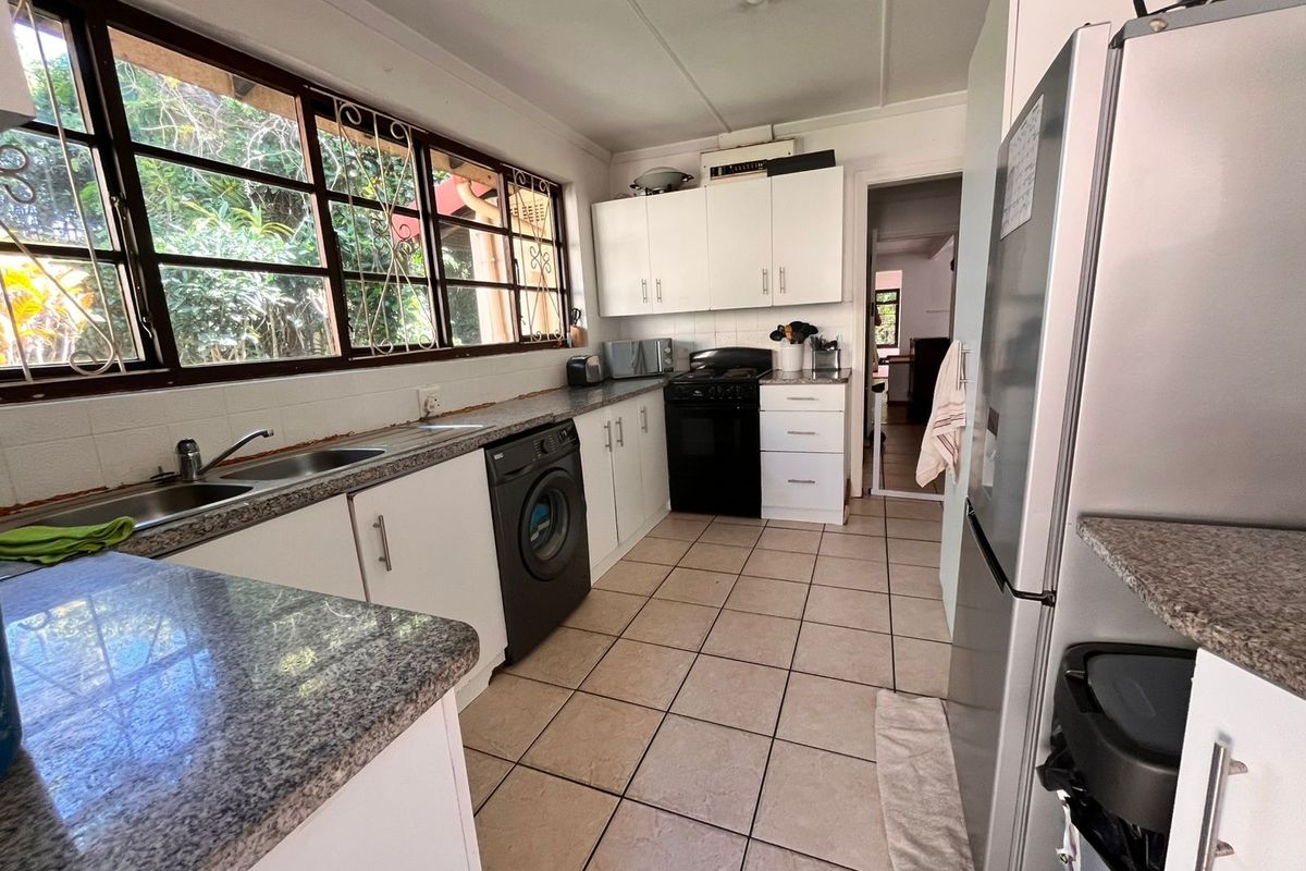 Functional kitchen featuring granite countertops, ample built-in cabinetry, double stainless steel sink, and ceramic tiled flooring with large windows providing natural light.