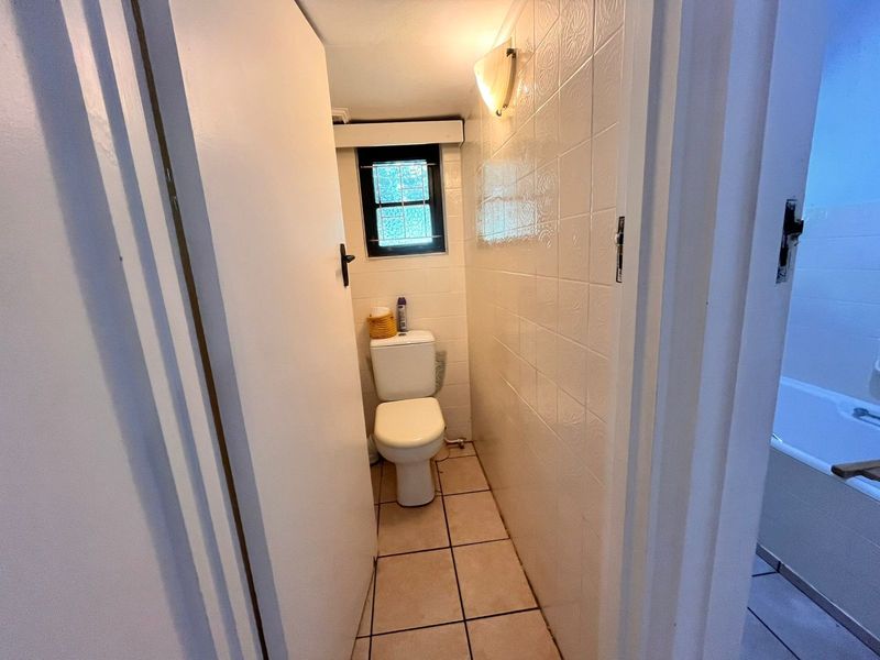 A compact, functional bathroom featuring tiled walls and flooring, a standard toilet, and a small window for natural light.