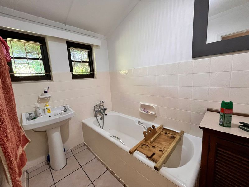 A functional bathroom featuring a pedestal basin, bathtub, and tiled finishes, offering potential for modernization and cosmetic updates.