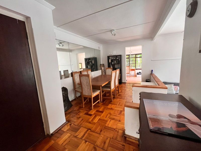 Dining area featuring classic parquet flooring, a large feature mirror, and an open-plan layout leading to an adjacent room.