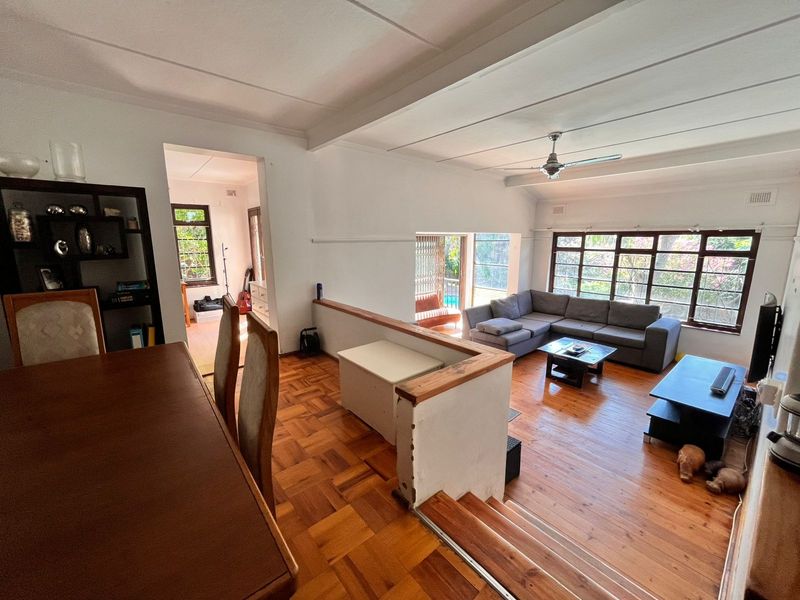 Spacious open-plan living and dining area featuring parquet and timber flooring, large multi-pane windows, and a split-level layout with a central partition wall.