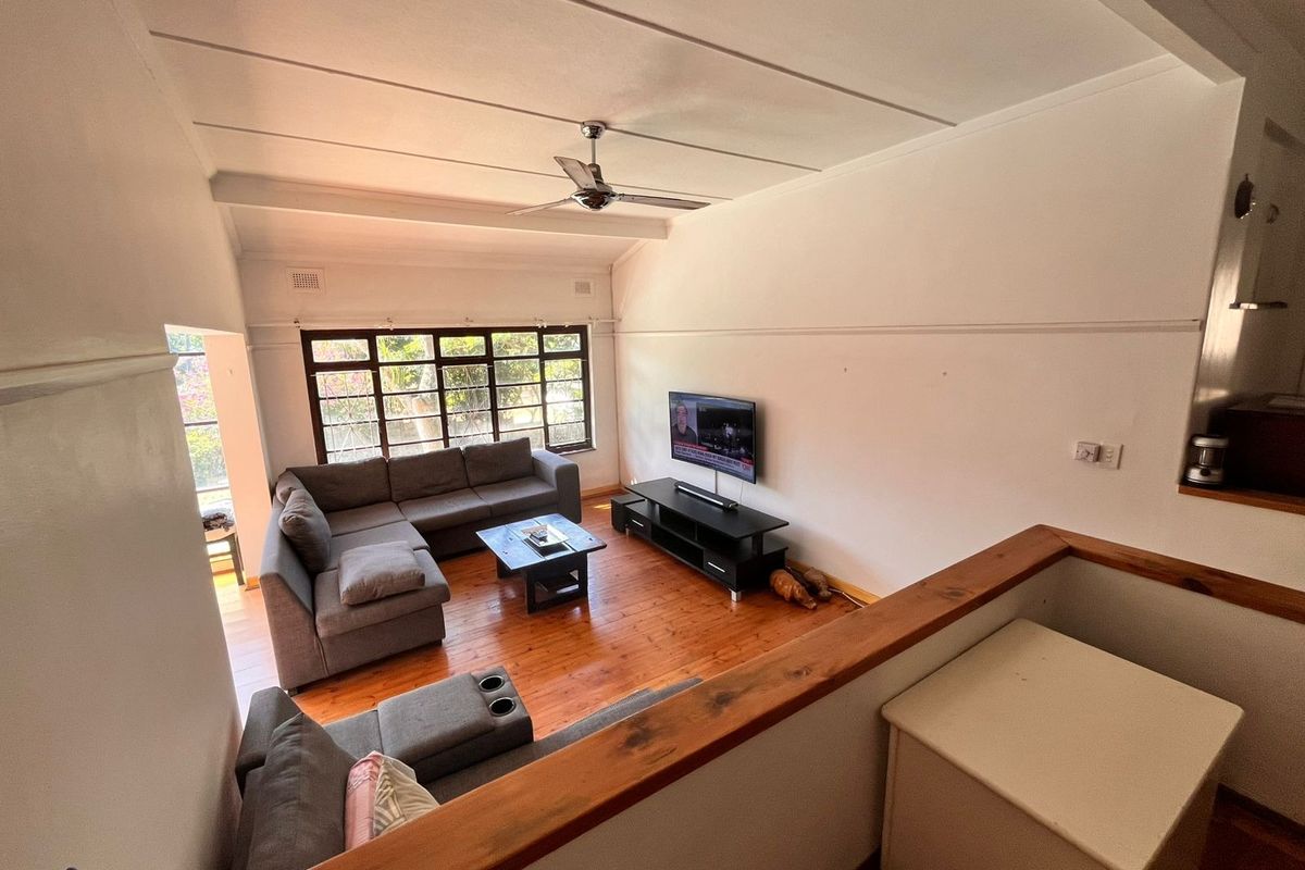 Spacious living room featuring polished timber flooring, a ceiling fan, and a large window providing natural light, viewed from an elevated mezzanine level.