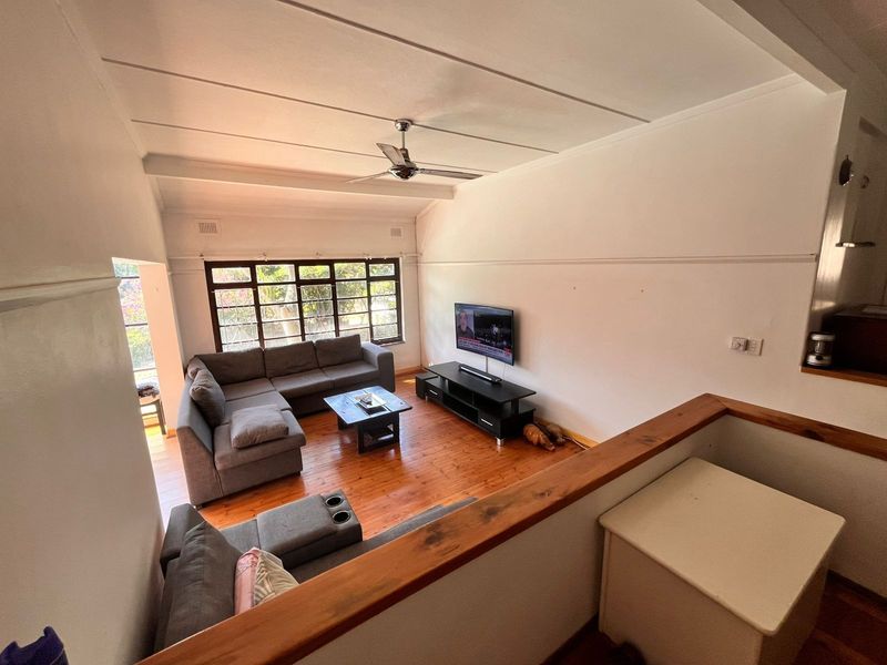 Spacious living room featuring polished timber flooring, a ceiling fan, and a large window providing natural light, viewed from an elevated mezzanine level.