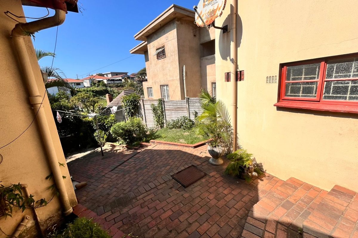 A rear exterior view showing a brick-paved patio area, boundary fencing, and the side elevation of the house with a satellite dish.