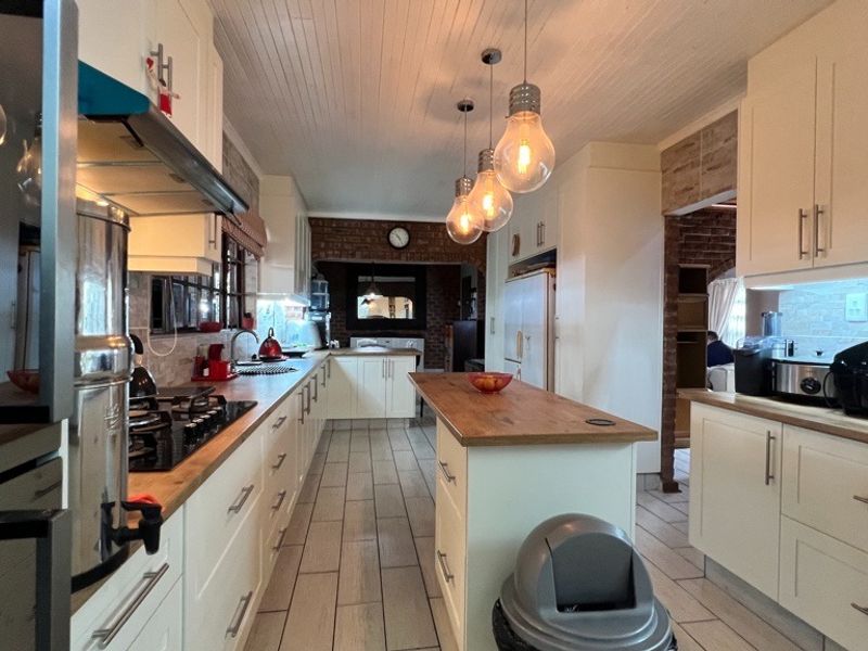A well-appointed kitchen featuring white cabinetry, wooden countertops, a gas hob, and stylish pendant lighting, complemented by exposed brick accents and tiled flooring.