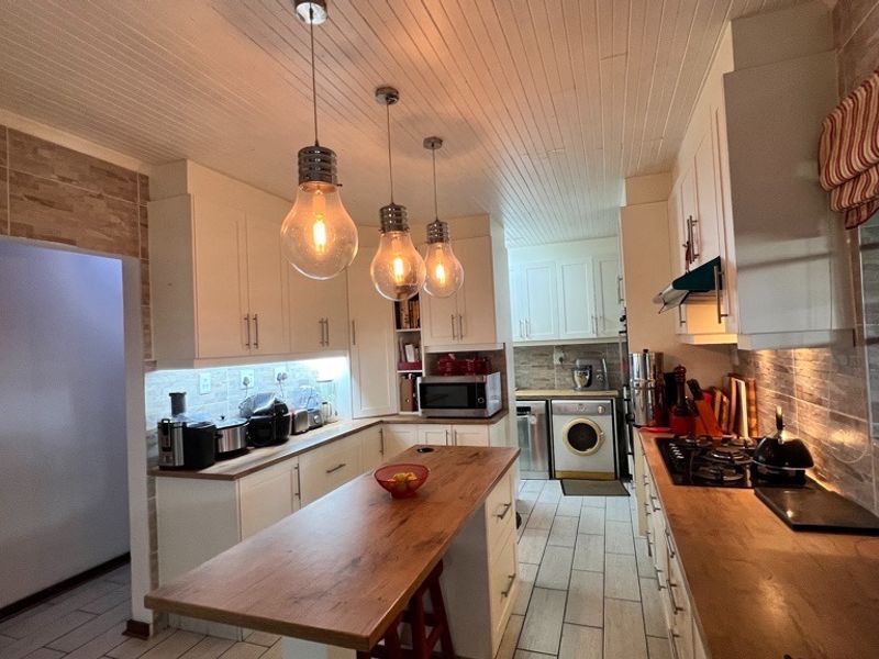 A well-appointed kitchen featuring white cabinetry, wooden countertops, a gas hob, and stylish pendant lighting, complemented by tiled flooring and a textured ceiling.