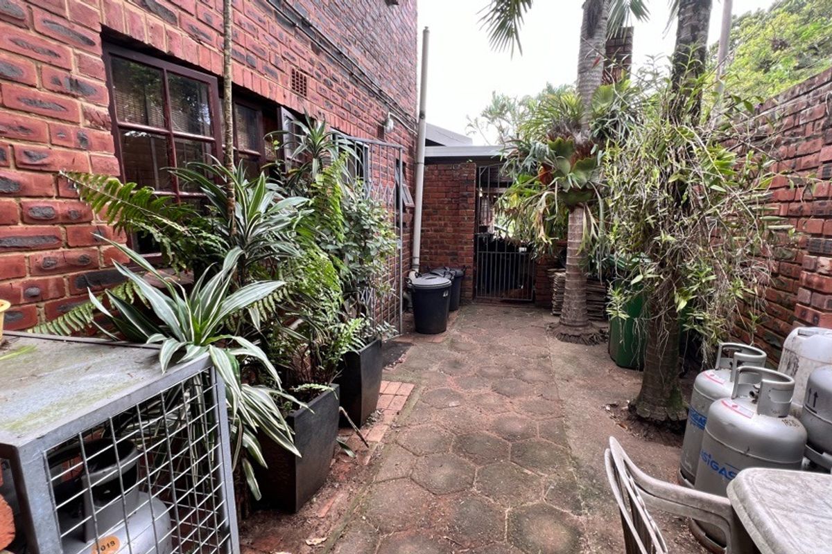 A side exterior walkway featuring exposed brick walls, paved flooring, and a secure metal gate leading to the rear garden area.