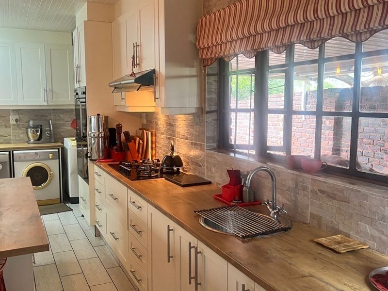 A well-maintained kitchen featuring white cabinetry, wooden countertops, a gas hob, built-in oven, and a tiled backsplash with a view to the exterior.