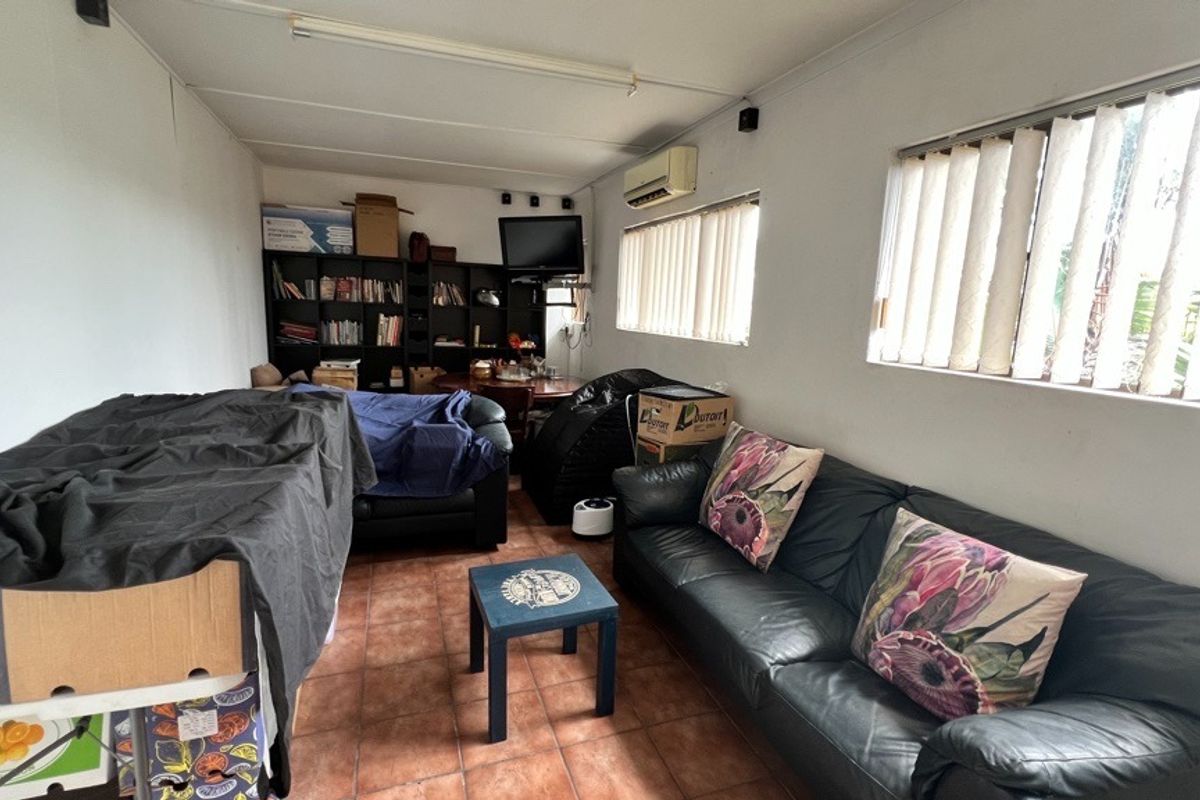 A living room featuring tiled flooring, vertical blinds, and a wall-mounted split-system air conditioner.