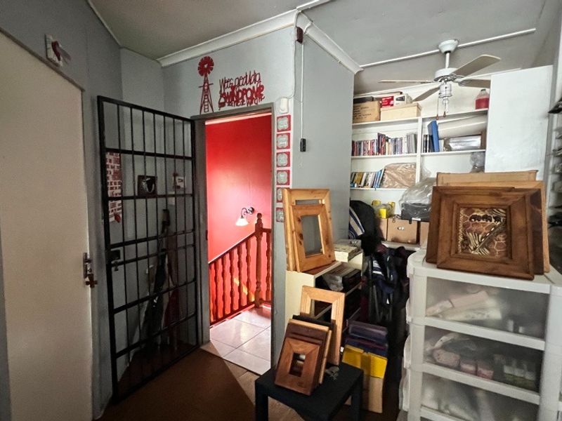 A functional hallway area featuring built-in shelving, a ceiling fan, and a security gate leading to a staircase.