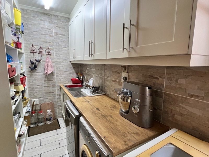 A functional scullery featuring built-in cabinetry, stone-look wall tiles, a timber-look countertop, and a stainless steel sink with ample open shelving.