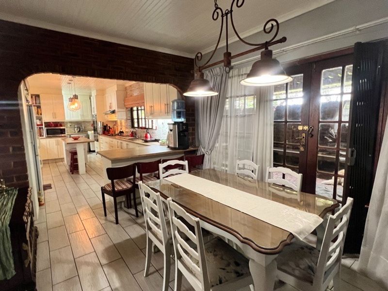 Open plan dining and kitchen area featuring exposed brick accents, tiled flooring, and direct access to the outdoor space through timber framed glass doors.