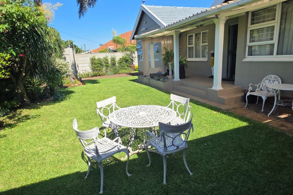 A well-maintained rear garden featuring a covered patio area with tiled flooring, support columns, and established landscaping.