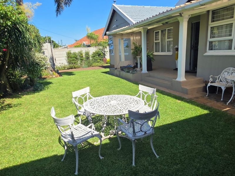 A well-maintained rear garden featuring a covered patio area with tiled flooring, support columns, and established landscaping.