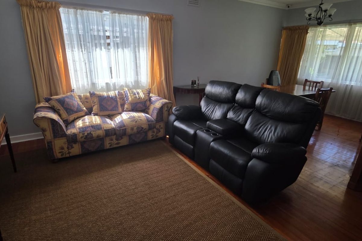 A living room featuring hardwood flooring, decorative cornice, and large windows with natural light.