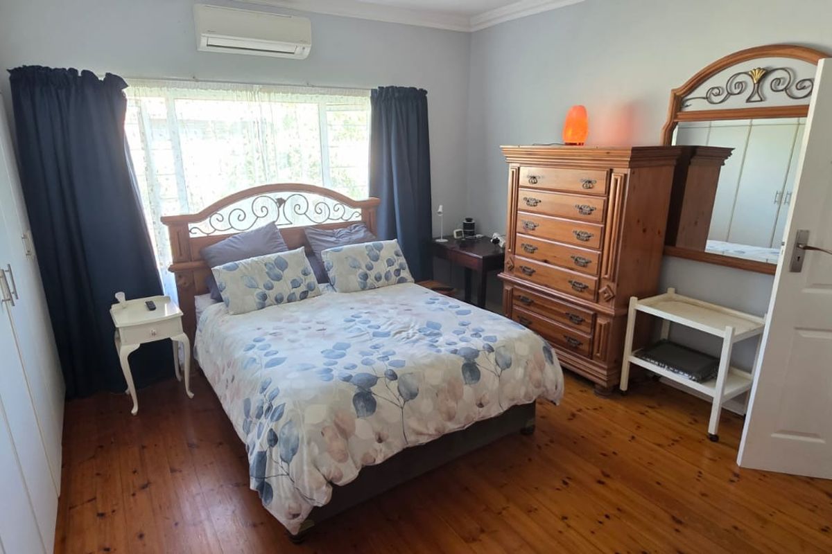 A well-proportioned bedroom featuring polished timber flooring, extensive built-in cupboard storage, and a wall-mounted air conditioning unit for climate control.